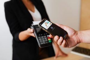 A person using a smartphone for contactless payment at a retail store counter. - How to Open a POS Business